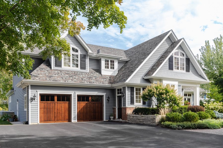 large two story blue house with wood garage doors and paved driveway